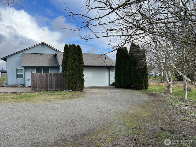 view of side of home featuring a garage, a shingled roof, driveway, and fence