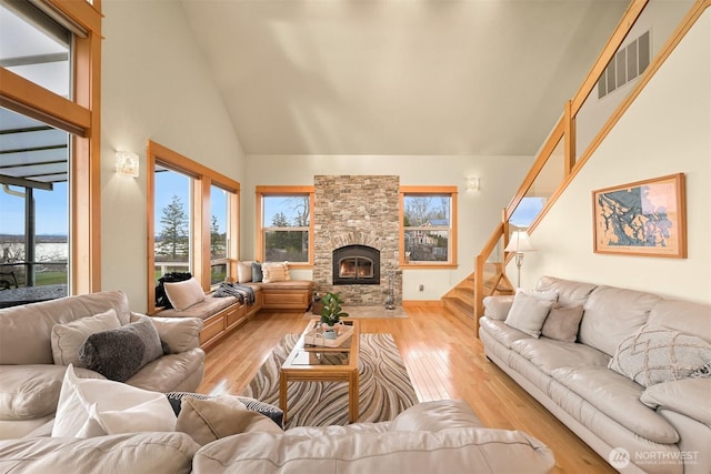 living room with high vaulted ceiling, a fireplace, visible vents, stairway, and light wood-type flooring