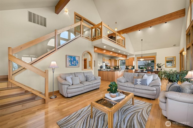 living room featuring light wood finished floors, visible vents, stairway, high vaulted ceiling, and beamed ceiling