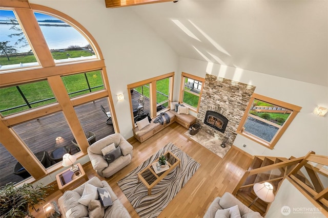 living room with a healthy amount of sunlight, high vaulted ceiling, wood finished floors, and a stone fireplace