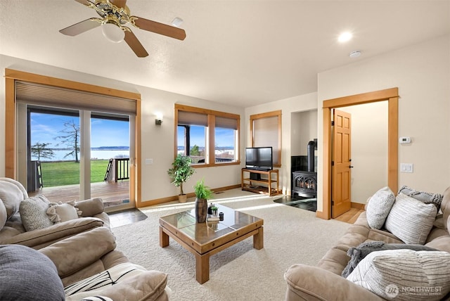 living area featuring a wood stove, a healthy amount of sunlight, baseboards, and a ceiling fan