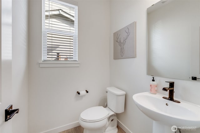 half bathroom featuring toilet, baseboards, and a sink