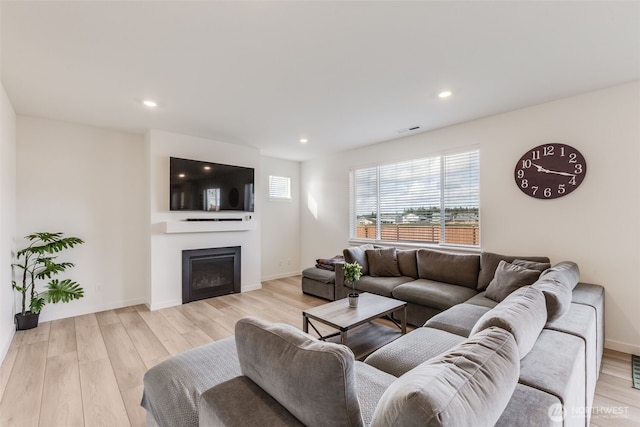 living room featuring a glass covered fireplace, visible vents, light wood-style flooring, and recessed lighting