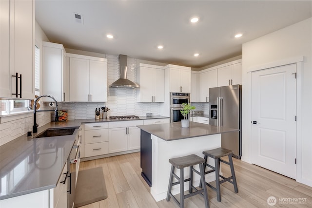 kitchen featuring stainless steel appliances, a sink, visible vents, light wood-style floors, and wall chimney exhaust hood