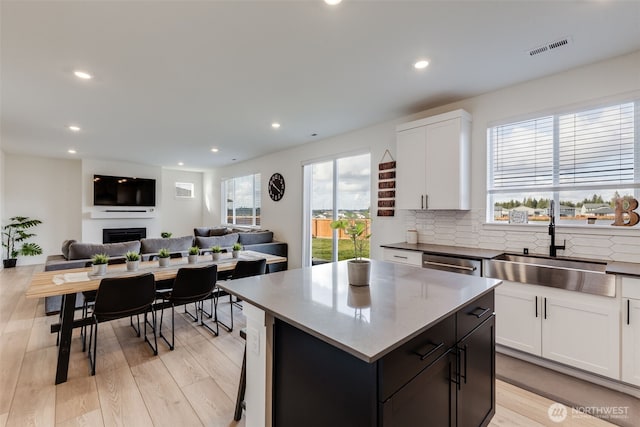 kitchen featuring a fireplace, a sink, visible vents, white cabinets, and open floor plan