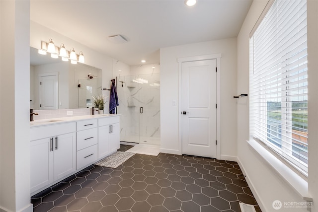 bathroom featuring a marble finish shower, double vanity, tasteful backsplash, a sink, and baseboards