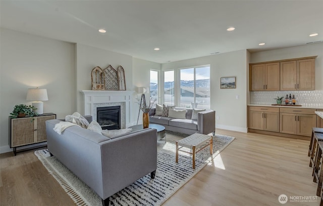 living room with a glass covered fireplace, baseboards, light wood-style flooring, and recessed lighting