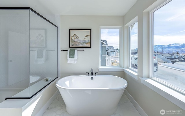 bathroom with marble finish floor, a mountain view, baseboards, and a freestanding tub