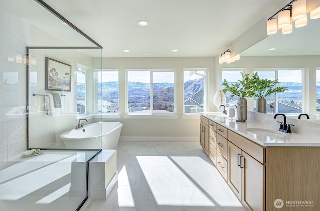 full bath featuring double vanity, recessed lighting, a freestanding tub, marble finish floor, and a sink