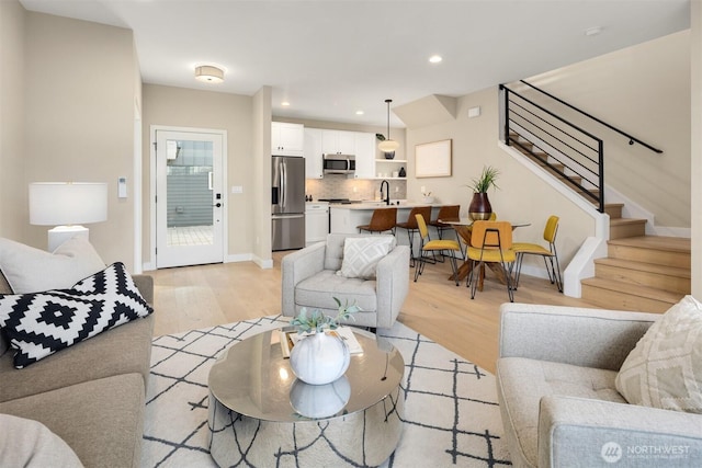 living area with light wood-style floors, baseboards, stairway, and recessed lighting