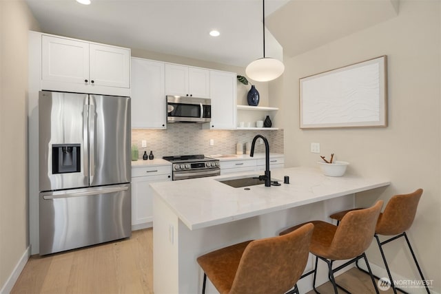 kitchen with decorative backsplash, appliances with stainless steel finishes, light wood-style floors, a kitchen bar, and a sink