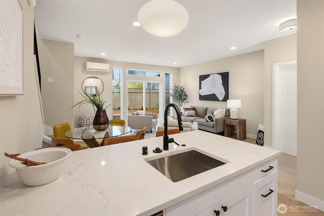 kitchen featuring light stone counters, recessed lighting, an AC wall unit, white cabinets, and a sink