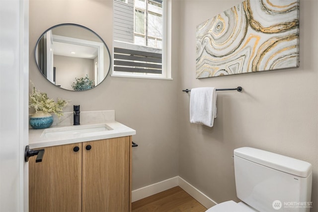 half bath with toilet, baseboards, wood finished floors, and vanity