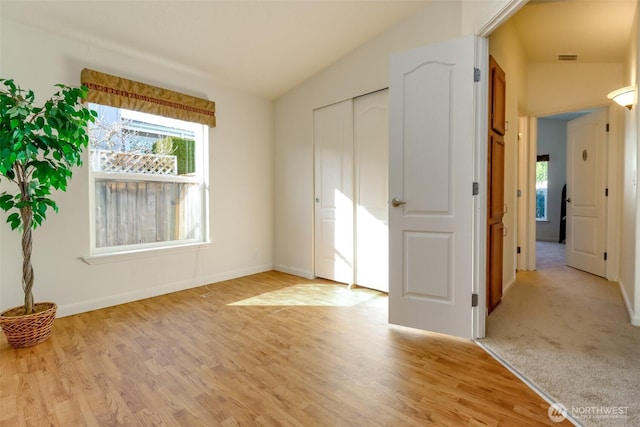 unfurnished bedroom with light wood-type flooring, baseboards, and vaulted ceiling