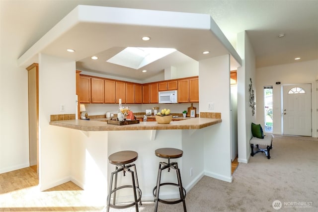 kitchen with a peninsula, white microwave, and brown cabinets