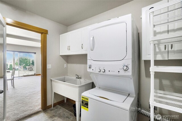 laundry area featuring carpet flooring, cabinet space, a sink, and stacked washer and dryer