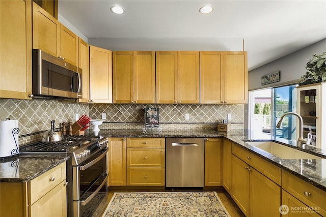 kitchen featuring light wood finished floors, backsplash, dark stone countertops, stainless steel appliances, and a sink