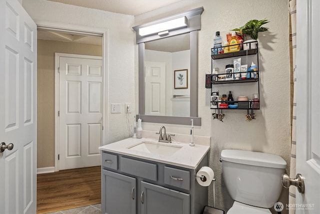 half bathroom with a textured wall, wood finished floors, vanity, and toilet