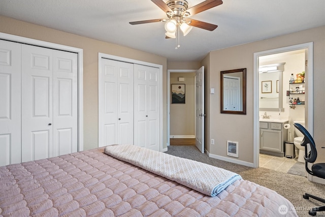 bedroom with multiple closets, ensuite bathroom, light carpet, a sink, and baseboards