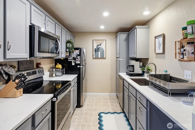 kitchen featuring stainless steel appliances, light countertops, gray cabinetry, a sink, and recessed lighting