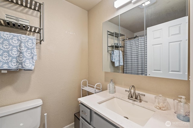 full bath featuring a textured wall, curtained shower, vanity, and toilet