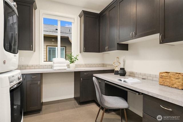 kitchen featuring stacked washer / dryer, light countertops, dark brown cabinetry, and light tile patterned floors