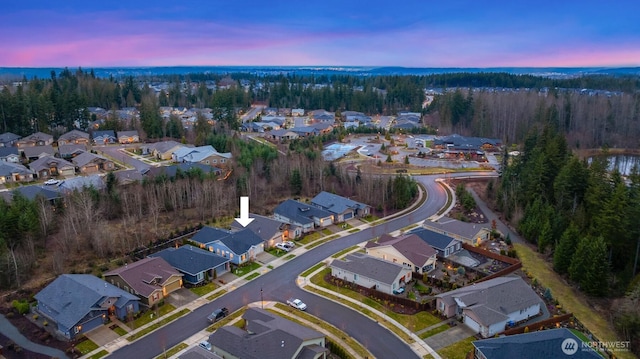 aerial view at dusk featuring a residential view and a wooded view