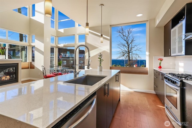 kitchen featuring a sink, light wood-style floors, appliances with stainless steel finishes, modern cabinets, and a glass covered fireplace