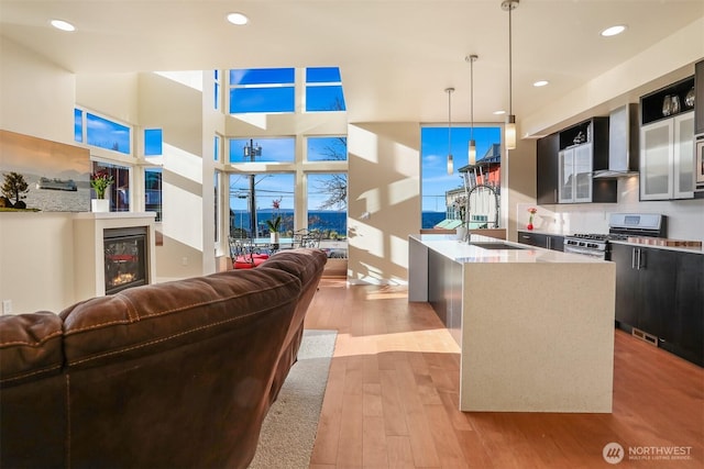 kitchen with light wood-style flooring, stainless steel gas stove, a sink, dark cabinetry, and wall chimney exhaust hood