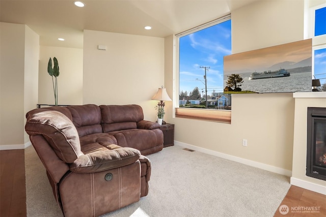 living area featuring baseboards, a glass covered fireplace, and recessed lighting