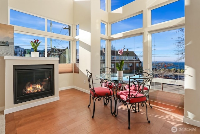 dining space featuring a glass covered fireplace, wood finished floors, a towering ceiling, and baseboards