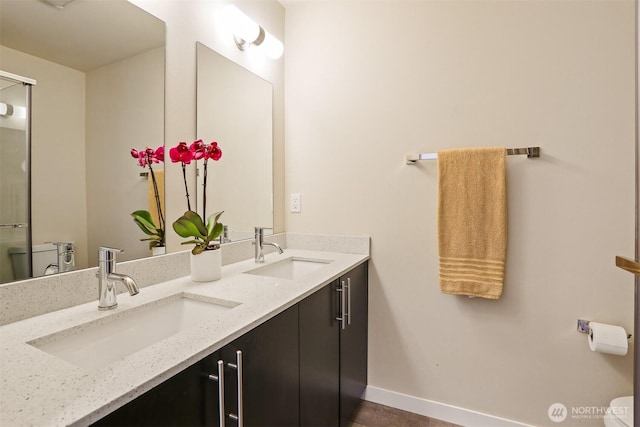 bathroom with toilet, a sink, baseboards, and double vanity