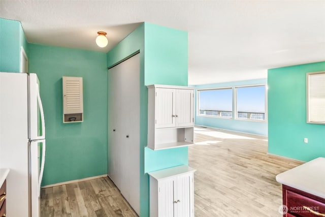 kitchen with freestanding refrigerator, white cabinets, light wood finished floors, baseboards, and light countertops