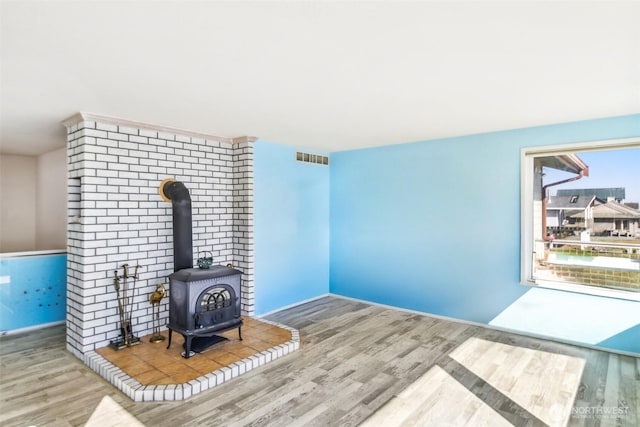 unfurnished living room with a wood stove, wood finished floors, and visible vents