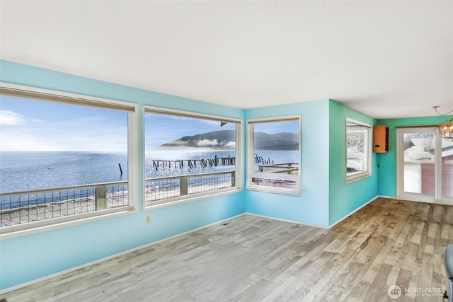 unfurnished room featuring a notable chandelier, wood finished floors, a water view, and baseboards