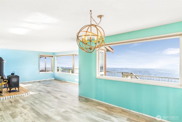 interior space with a chandelier, a wood stove, baseboards, and wood finished floors