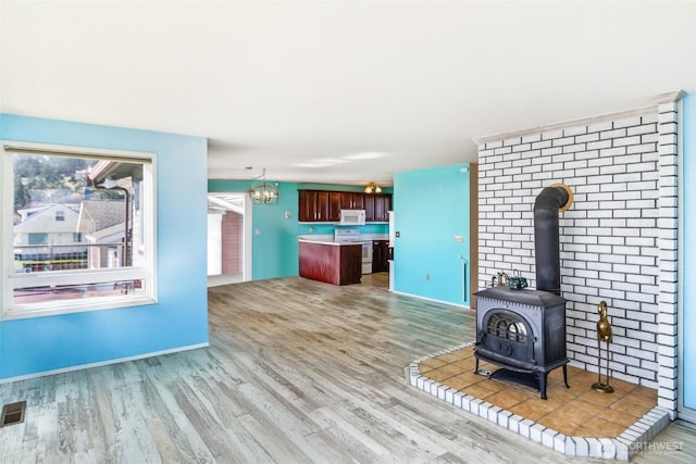 unfurnished living room with visible vents, baseboards, an inviting chandelier, a wood stove, and light wood-style floors