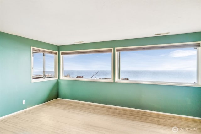 unfurnished room with visible vents, plenty of natural light, wood finished floors, and a water view