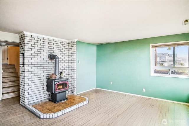 unfurnished living room with visible vents, baseboards, stairs, a wood stove, and wood finished floors