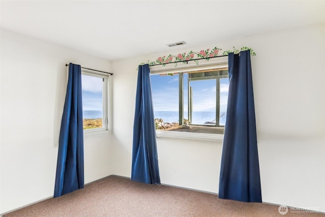 unfurnished room with visible vents, a water view, and carpet flooring