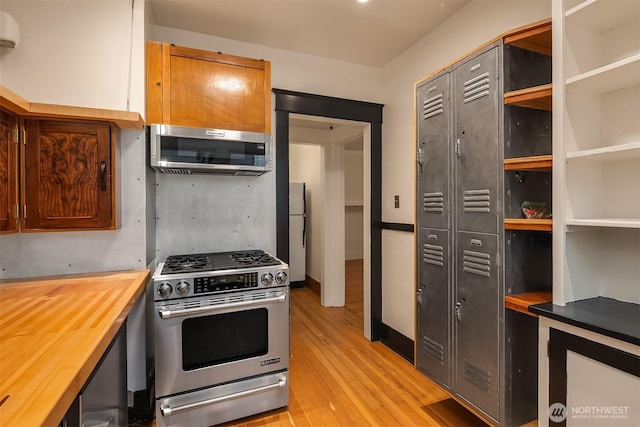 kitchen with appliances with stainless steel finishes, a wall mounted air conditioner, light wood-style floors, and wood counters