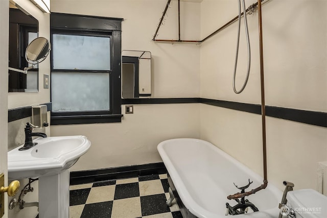 bathroom featuring a sink, baseboards, a freestanding bath, and tile patterned floors