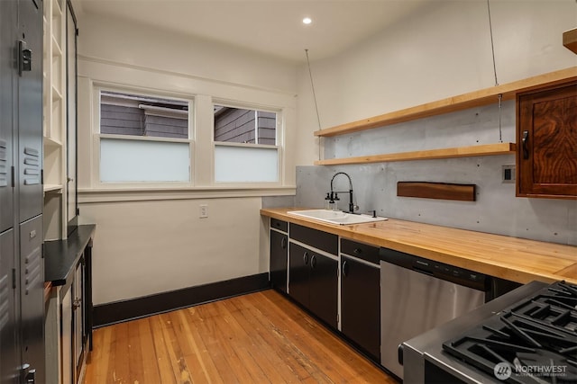 kitchen with butcher block counters, light wood-style floors, a sink, dishwasher, and baseboards