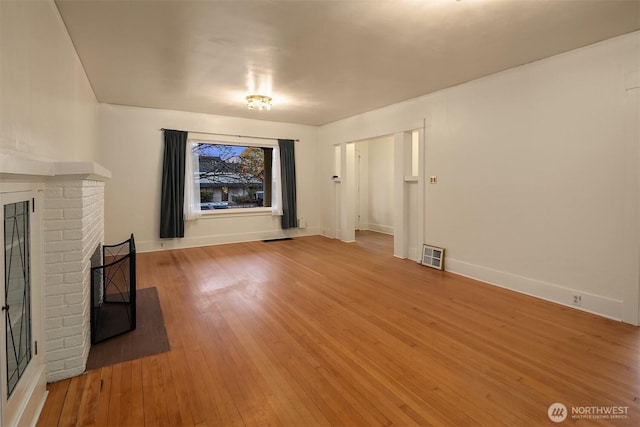 unfurnished living room with wood-type flooring, a fireplace, visible vents, and baseboards