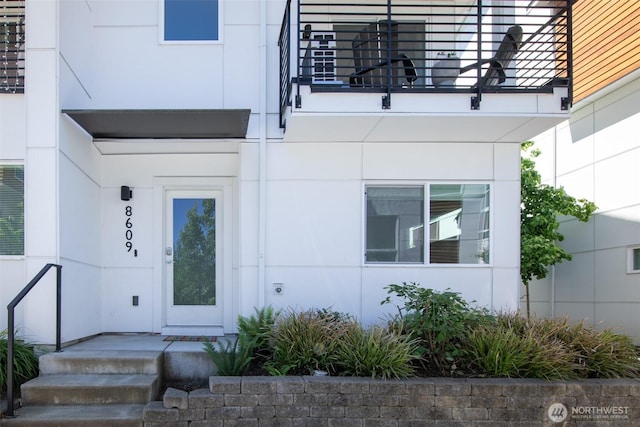 view of exterior entry with a balcony and stucco siding