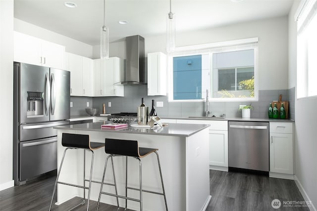 kitchen featuring a breakfast bar area, a center island, stainless steel appliances, wall chimney range hood, and a sink