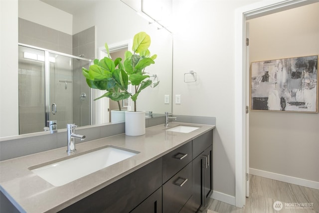 bathroom featuring double vanity, a shower stall, baseboards, and a sink