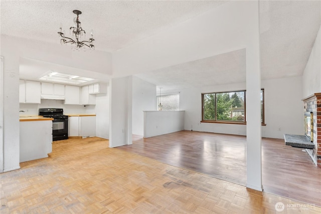 unfurnished living room featuring a brick fireplace, a textured ceiling, parquet floors, and an inviting chandelier