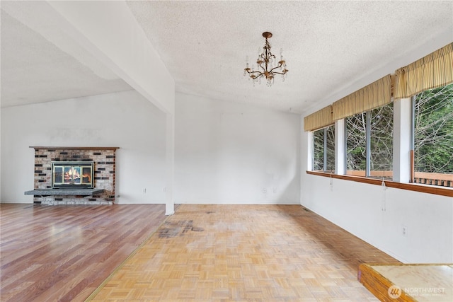 unfurnished living room with a textured ceiling, a fireplace, a chandelier, vaulted ceiling, and parquet flooring