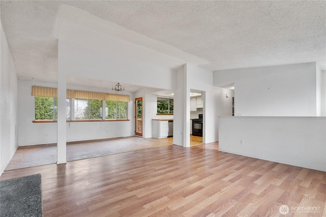 unfurnished living room featuring an inviting chandelier, a textured ceiling, light wood-style floors, and vaulted ceiling